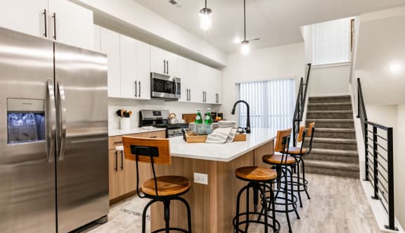 an open kitchen with a counter with bar stools and a stainless steel refrigerator