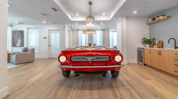 A red vintage car is parked in a modern living room.