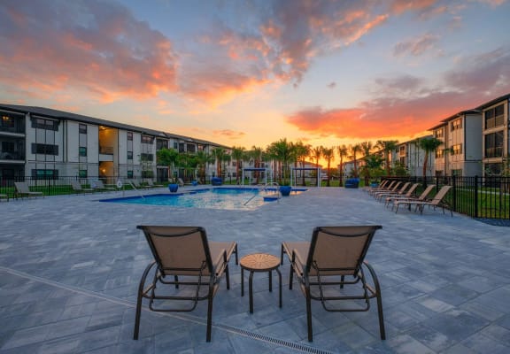 an outdoor patio area with chairs and a pool at sunset