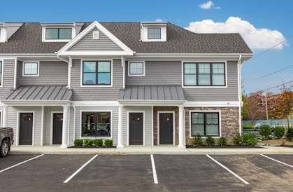 A grey building with a parking lot in front.