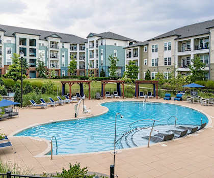 A large swimming pool surrounded by lounge chairs and umbrellas in front of apartment buildings. at TRAILSIDE VERDAE Apartments , GREENVILLE, South Carolina