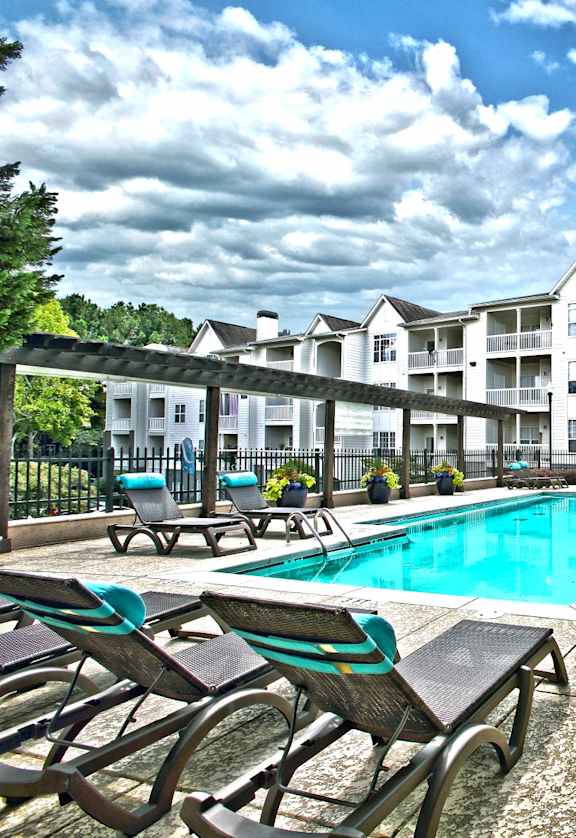 A pool area with chairs and a table with a yellow umbrella.