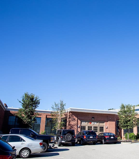 Parking area with brick buildings and trees at Star Mill Lofts Apartments, Middleboro