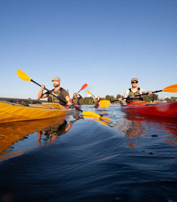 Three people kayaking on a calm body of water.