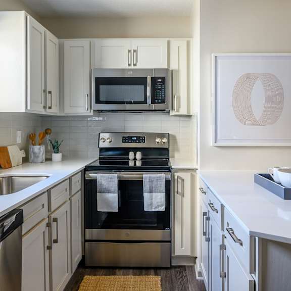 The cozy kitchen at one of the apartments with stainless steel appliances, white counters, and white cabinets,at Retreat at McAlpine Creek Apartments with a sink, dishwasher, counters, oven, microwave, and utensils. 