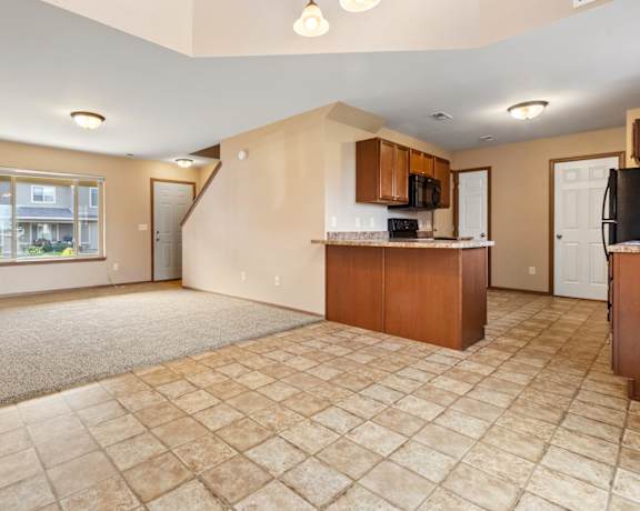 A spacious living room with a kitchen area in the background.