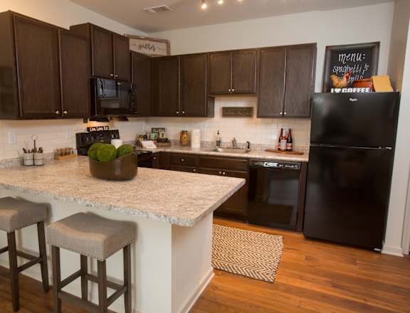 A kitchen with dark brown cabinets and a black fridge.