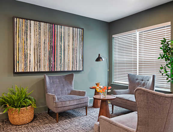 A living room with a grey chair, a brown table, and a large picture on the wall.