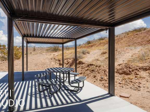 A metal patio structure with a table and chairs in a desert landscape.