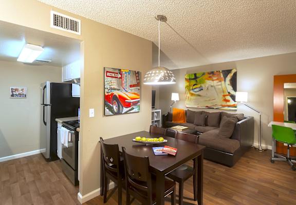 A kitchen with a refrigerator, oven, and a dining table with chairs.