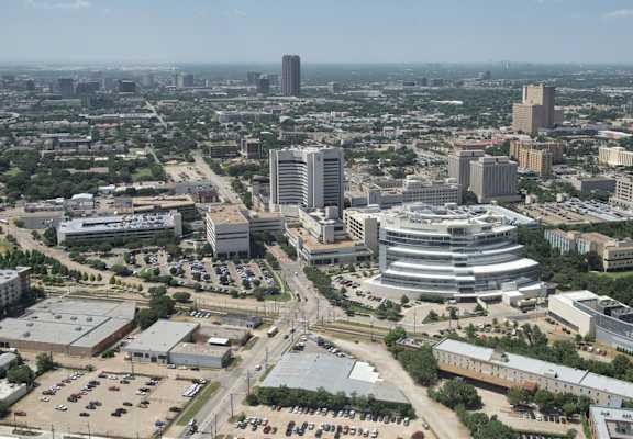 A cityscape with a mix of modern and older buildings, surrounded by greenery and roads.