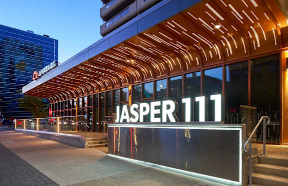 A modern building with a glass facade and a wooden structure above the entrance.