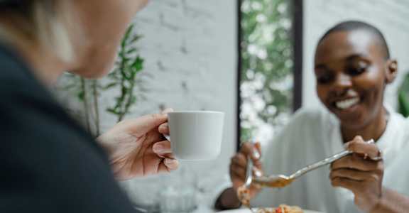 A person is eating spaghetti with a fork and a cup of coffee.