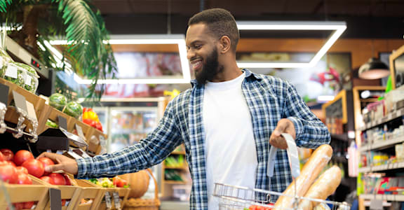 A man is shopping in a grocery store, picking out apples and placing them in his basket.
