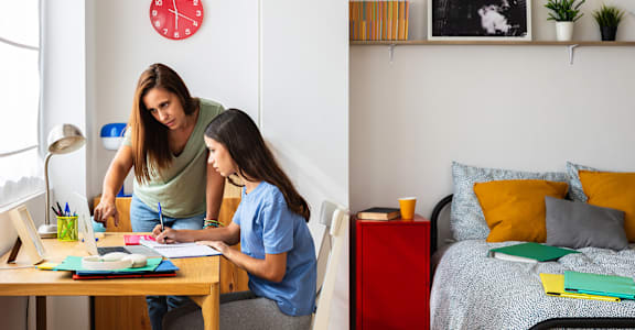 A woman and a girl are sitting at a table with books and papers.