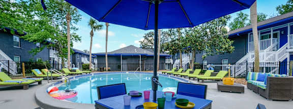 A blue table with matching chairs and an umbrella is set up in a courtyard with a pool.