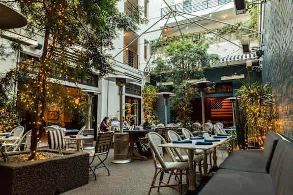 A restaurant with tables and chairs is surrounded by greenery and has a warm, inviting atmosphere.