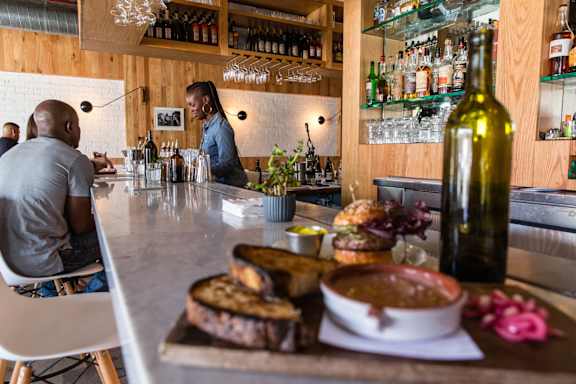 A man is sitting at a bar with a bottle of wine and a plate of food in front of him.