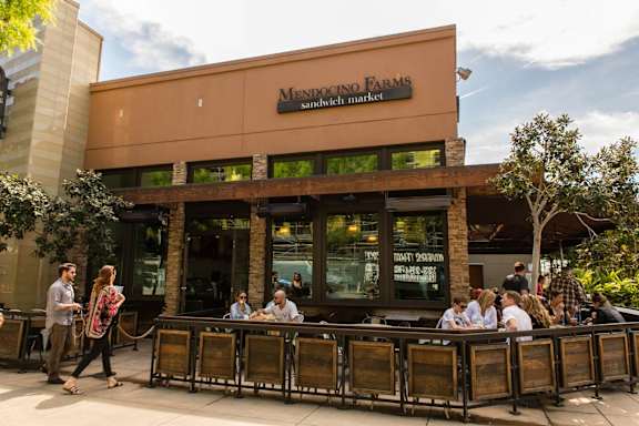 A group of people are sitting at a bar outside of Mendocino Farms.