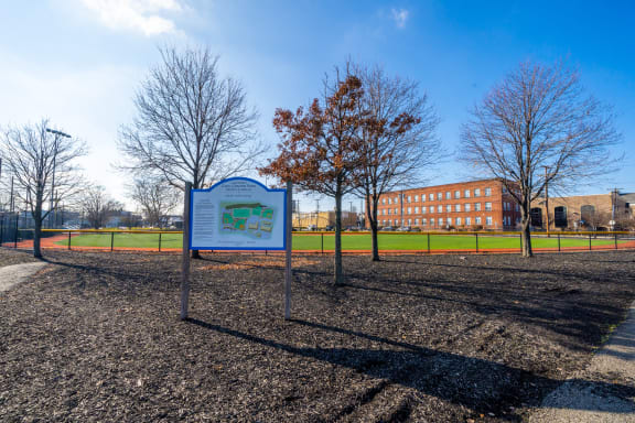 a park with a sign and a building in the background at The Botanic, Carteret, NJ, 07008