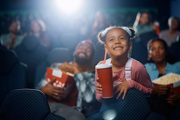 Young girl is smiling and holding a drink and popcorn while watching a movie in a theater at The Bosk Apartment Homes, Minnesota
