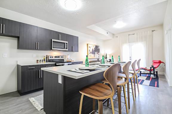 A kitchen with a white counter top and wooden chairs.