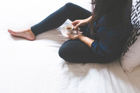 a woman sitting on a bed holding a cup of coffee