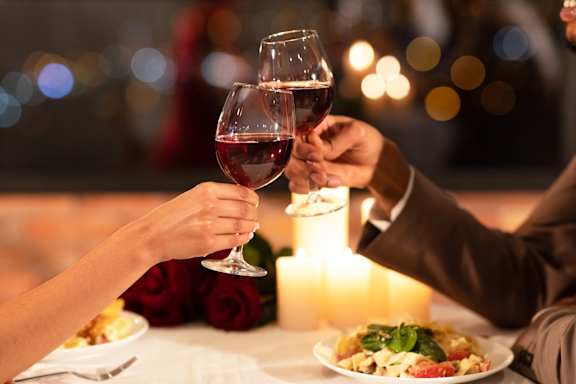 Two people toasting with wine glasses in front of a candlelit table.