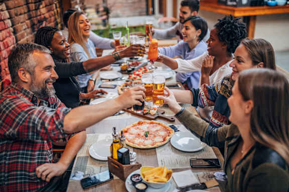 A group of people toasting with beer glasses at a table with food.