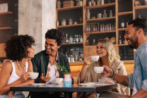 Four people are having a conversation over coffee in a cozy café setting.