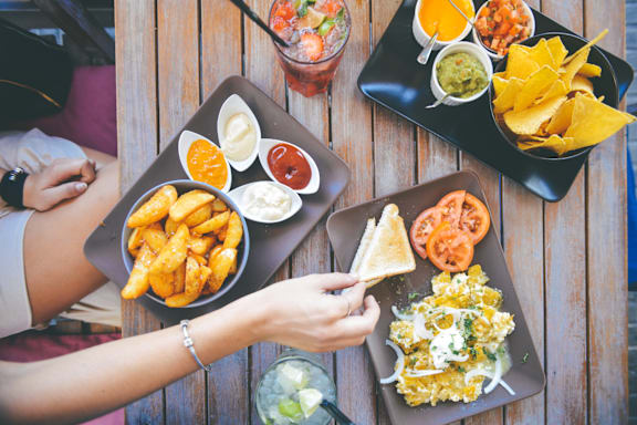 A person is eating a meal consisting of nachos, guacamole, salsa, and other sides.