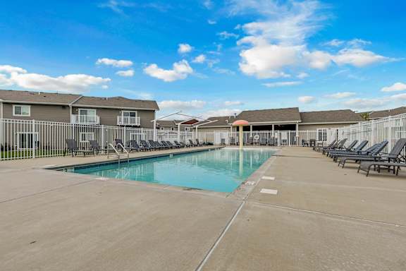 A large swimming pool surrounded by lounge chairs and apartment buildings.