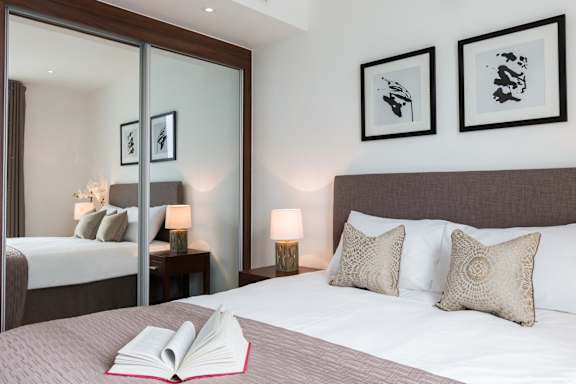 A bedroom with a large bed, a book on the bed, and two framed pictures on the wall.