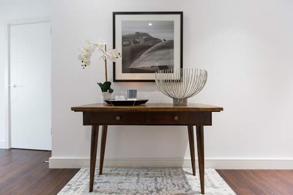 a small wooden table with a vase and a picture on the wall above it