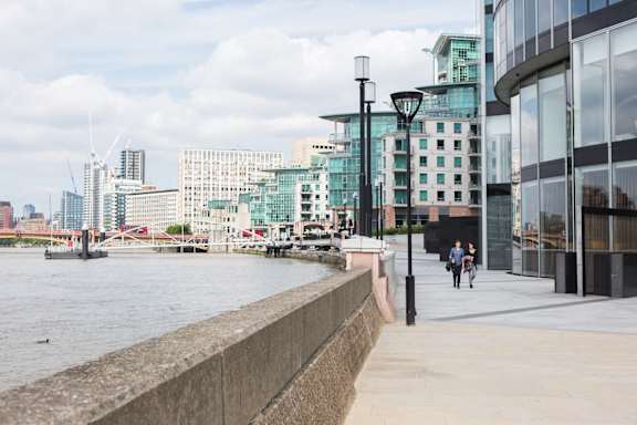 people walking along the river with buildings in the city