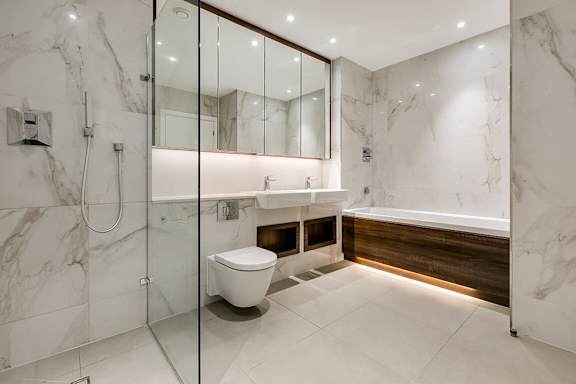 the ensuite bathroom has marble walls and flooring and a glass shower and toilet