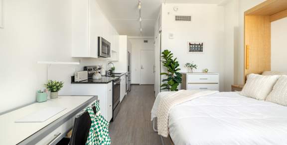 A white bedroom with a bed, desk, and shelves.