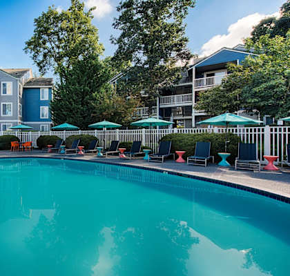 a swimming pool with chairs and umbrellas in front of an apartment building