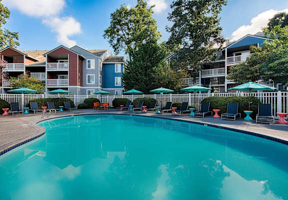 a swimming pool with chairs and umbrellas in front of an apartment building