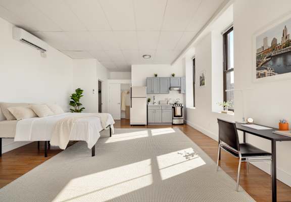 A well-lit room with a bed, a desk, and a chair.