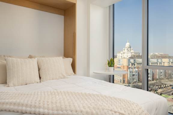 A bedroom with a large bed and a view of a cityscape through the window.