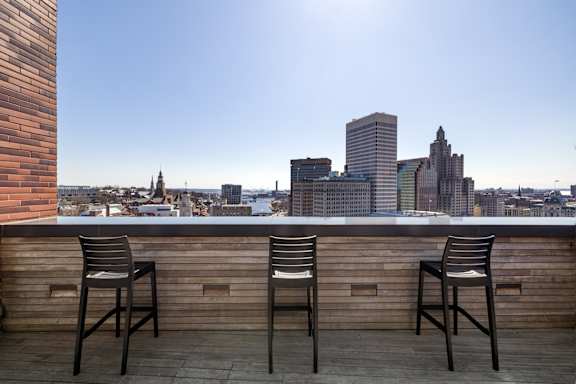 Three chairs are placed on a wooden deck with a city skyline in the background.