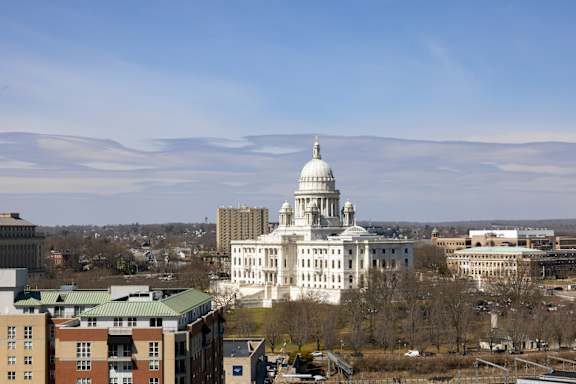 A large white building with a dome on top is in the center of a cityscape.