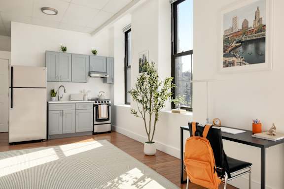 A kitchen with a white fridge and a white table with a black chair and an orange backpack on it.