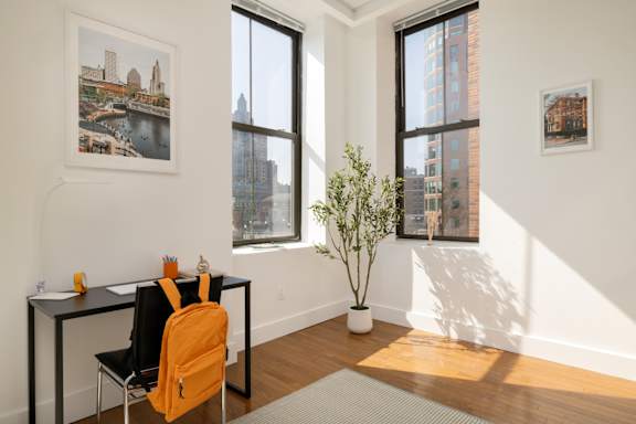 A room with a desk, chair and a potted plant.