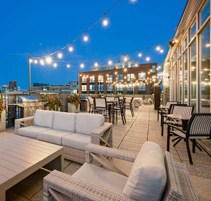 a rooftop terrace with couches and tables and a city at night