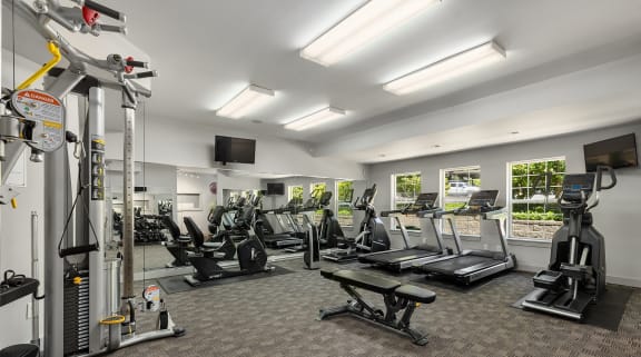 a gym with cardio equipment and weights in a room with windows