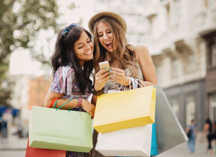 two women with shopping bags looking at a cell phone