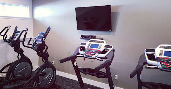 a room with three exercise machines and a tv on the wall