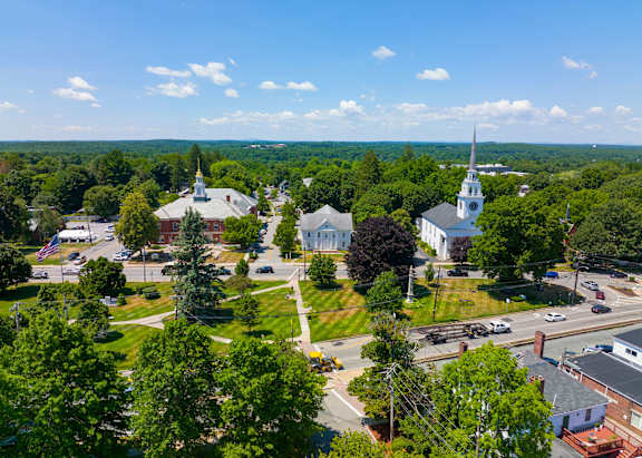 A church with a tall steeple stands in a town surrounded by trees.